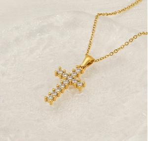 Detailed close-up of golden cross pendant with sparkling zircons on a glass plate