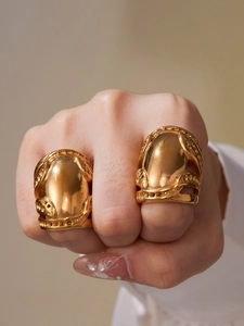Macro shot of two oversized gold shield rings with intricate embossed patterns on fingers