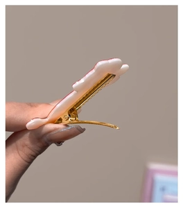 Detail of cute pink and white resin cloud hair clip with golden metal crocodile grip