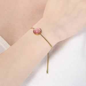 Détail d'une pierre naturelle rose sur un bracelet chaîne serpent doré au poignet