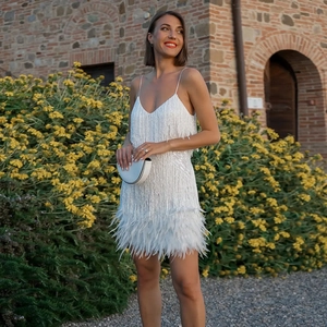 Détail de robe blanche à paillettes avec col en V, franges et plumes élégantes
