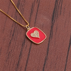 Close-up of golden necklace featuring a red square pendant with a sparkling diamond heart