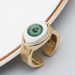Detail of adjustable gold ring featuring a green evil eye motif and textured metal finish