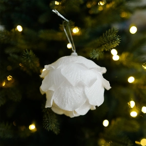 White glitter petal Christmas ball ornament hanging on a festive tree with warm bokeh lights