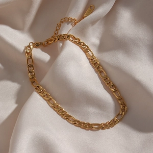 Macro shot of 18K gold plated Figaro chain necklace with lobster clasp on white silk