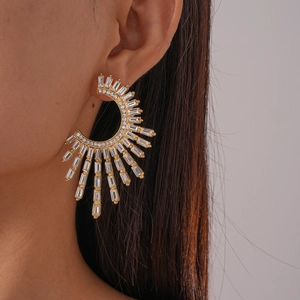 Close-up of geometric C-shaped gold earrings with sparkling crystals on female ear