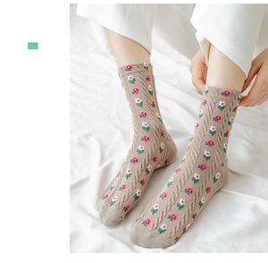 Close-up of beige knit crew socks with small red floral patterns and cable knit texture