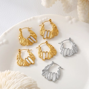 Irregular 18k gold and silver shell earrings with wave textures on a white ceramic plate