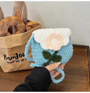 Detail of blue crochet kids bag with pink flower and knitted strap on a wooden tray