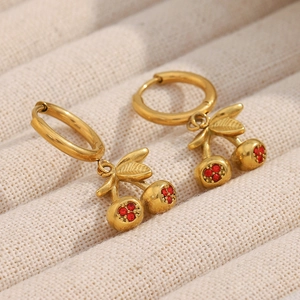 Macro detail of 18K gold-plated cherry earrings with red rhinestones on soft fabric