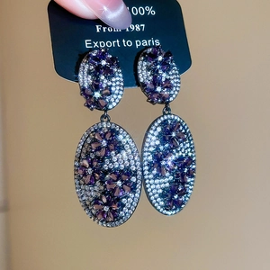 Macro detail of oval vintage earrings with purple floral pattern and sparkling zircon stones