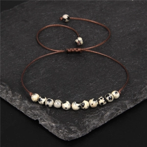 Adjustable 4mm Dalmatian Jasper beaded woven bracelet on natural black rock surface