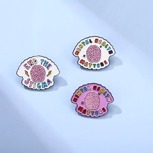 Macro view of three mental health awareness enamel pins on light blue background