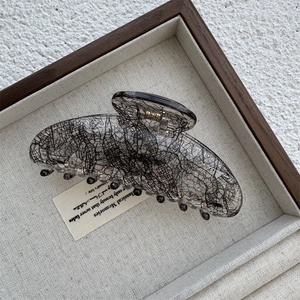 Close-up of a high-quality acrylic hair claw with vintage black mesh patterns and golden spring