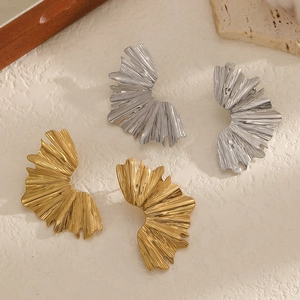 Minimalist 18k gold and silver pleated leaf earrings on beige stone textured surface