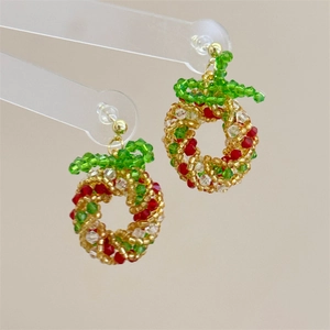 Macro shot of handmade beaded Christmas wreath earrings with festive red and gold accents