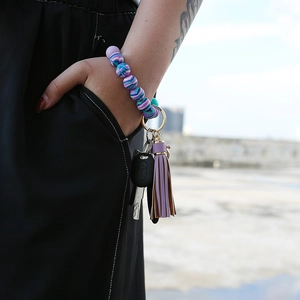 Close-up of silicone beaded wristlet keychain with purple tassel and gold ring on wrist