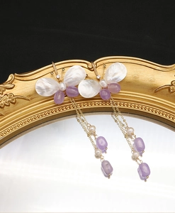 Detailed view of butterfly earrings with pearls and purple beads on golden chains