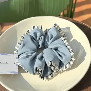 Detailed close-up of blue pleated scrunchie with striped edges on a white plate
