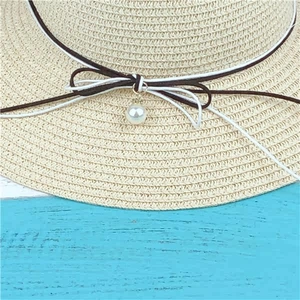 Detailed view of beige straw hat featuring black and white bow with elegant pearl pendant