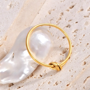 Close-up of minimalist gold knot ring resting on a textured stone and white pearl