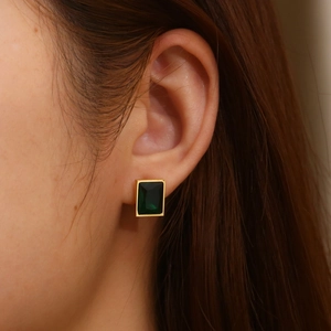 Gros plan de boucles d'oreilles dorées avec pierres précieuses rectangulaires vert émeraude
