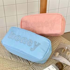 Close-up of pink and light blue nylon makeup bags with honey towel embroidery detail