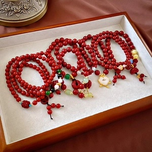 Détail de bracelets en perles de cinabre avec breloques dorées sur plateau en bois