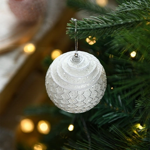Close-up of a white glitter Christmas ball with wave textures on a green pine tree