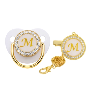 Detail of golden baby pacifier and clip set featuring sparkling rhinestones and letter M