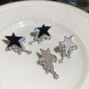 Close-up of star-shaped stud earrings with zircon inlay and black or white shell centers