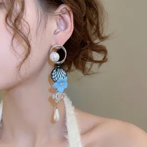 Elegant drop earrings featuring pearls, blue flowers, and crystals worn by a model