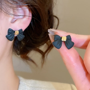 Close-up of black matte bow earrings with golden metal center on model ear