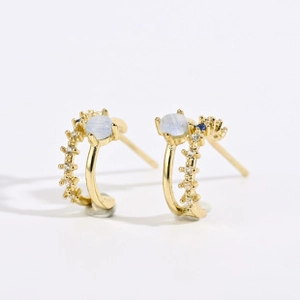 Detail of 18k gold C-shape earrings with light blue moonstone and zircon pavé accents