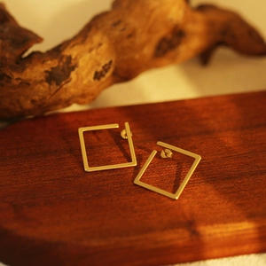 Close-up of minimalist golden square hollow stud earrings on a dark wooden surface