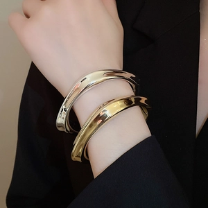 Détail de bracelets métalliques elliptiques dorés et argentés portés au poignet