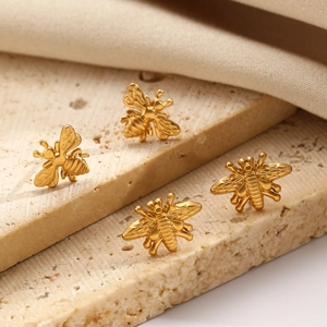 Macro shot of four golden bee earrings on a textured stone surface showing wing details