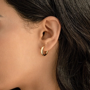 Close-up of small polished gold hoop earring worn on ear for a minimalist look