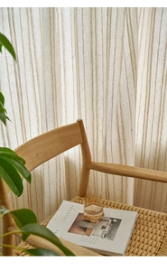 Close-up of beige linen stripe curtains with natural light and a wooden rattan chair