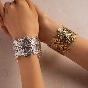 Detail of wide open cuff bracelets in gold and silver with intricate hollow floral patterns
