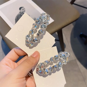 Handheld view of two elegant oval hair clips with sparkling clear zircons on a white card