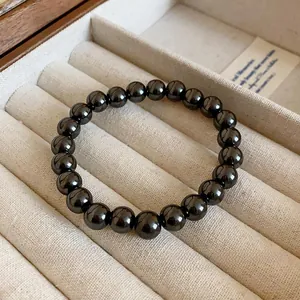 Gros plan d'un bracelet de perles noires polies sur un présentoir en velours beige