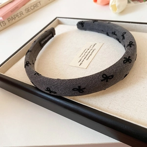 Detail of grey padded headband with black bow patterns and handmade label on a box