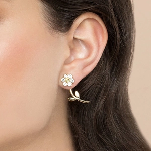 Detailed close-up of a golden flower and leaf earring with crystals on a female model