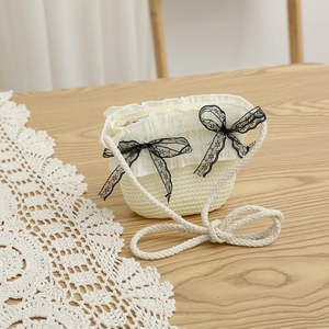 Détail du sac bandoulière en paille crème avec bordure en dentelle et nœuds noirs