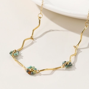 Golden wavy link necklace with multicolored beads on a minimalist cream background