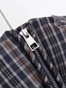 Close-up of metal zipper detail on plaid jacket with grey and brown woven fabric texture