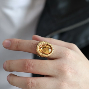 Detailed macro view of woven gold texture and amber oval gemstone on stainless steel ring