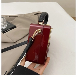 Detail of wine red patent leather box bag featuring gold hardware and black handle