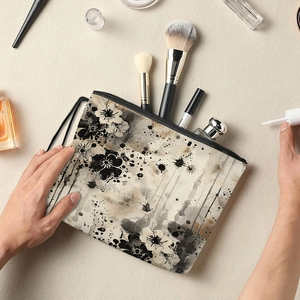 Ink floral canvas cosmetic bag with black zipper and wrist strap shown in use
